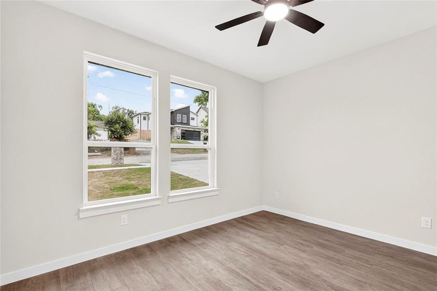 Bright room featuring two large windows, wood-finish flooring, a ceiling fan with integrated lighting, and neutral wall paint