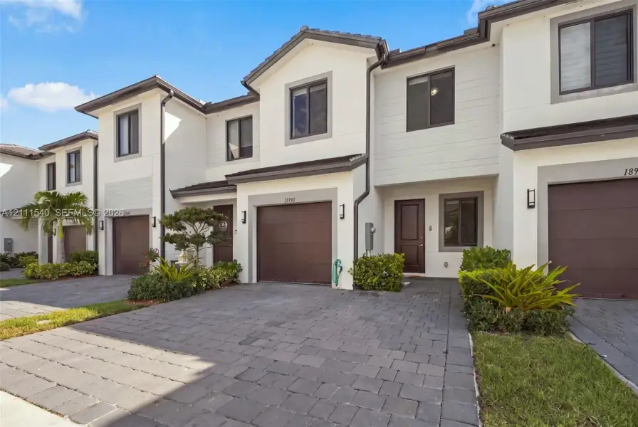Multi-level townhouse exterior featuring a paver driveway, an attached garage, and a light-toned stucco façade