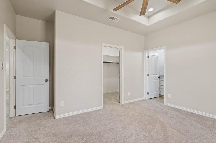 Unfurnished bedroom featuring ceiling fan, light colored carpet, a walk in closet, and ensuite bath Unfurnished bedroom featuring ceiling fan, light colored carpet, a walk in closet, and ensuite bath
