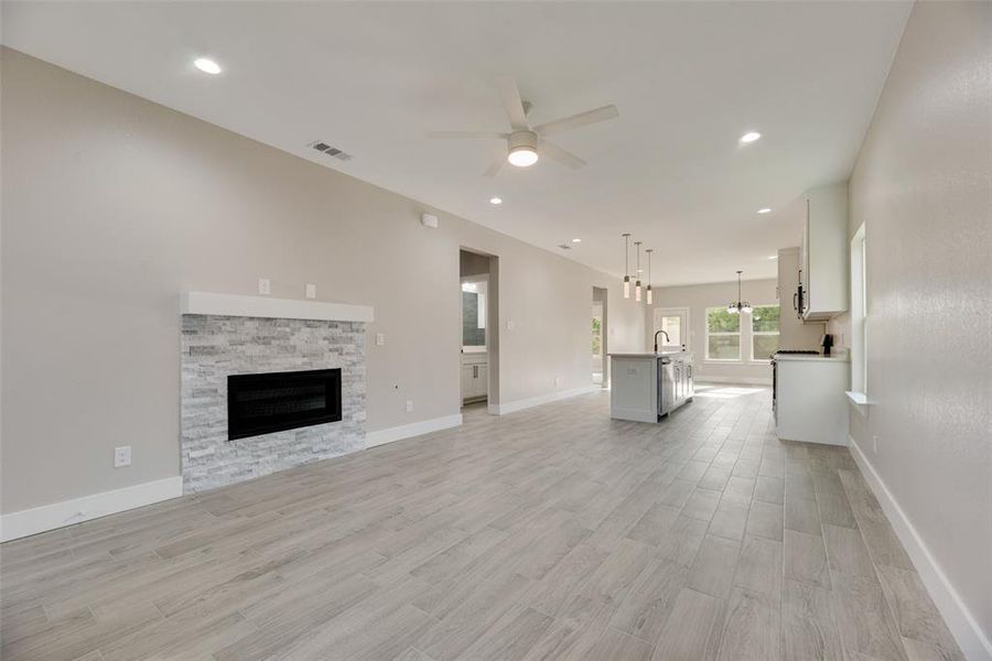 Unfurnished living room featuring a stone fireplace, sink, ceiling fan, and light ceramic tile hardwood / wood-style floors