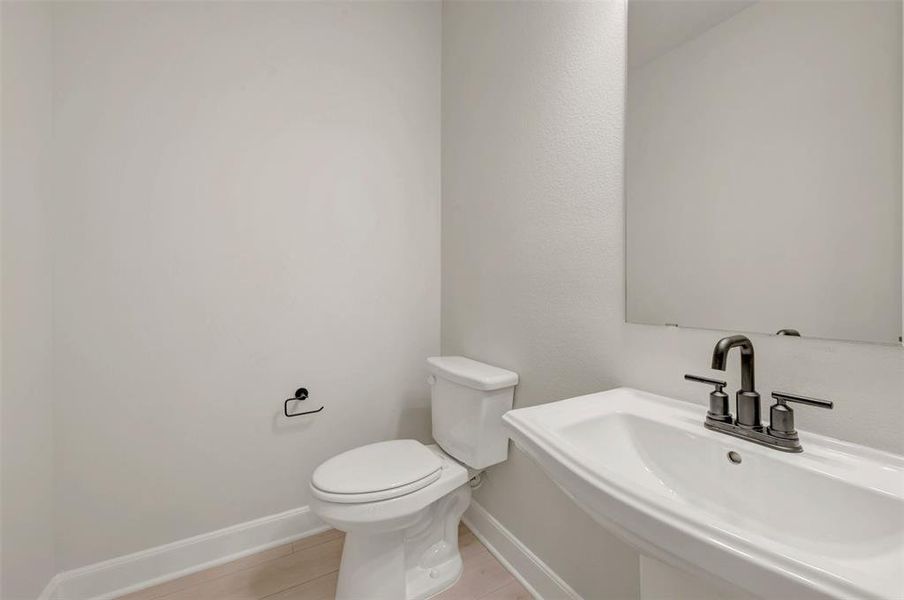 Contemporary pedestal sink with a matte black faucet, wall-mounted mirror, and white toilet