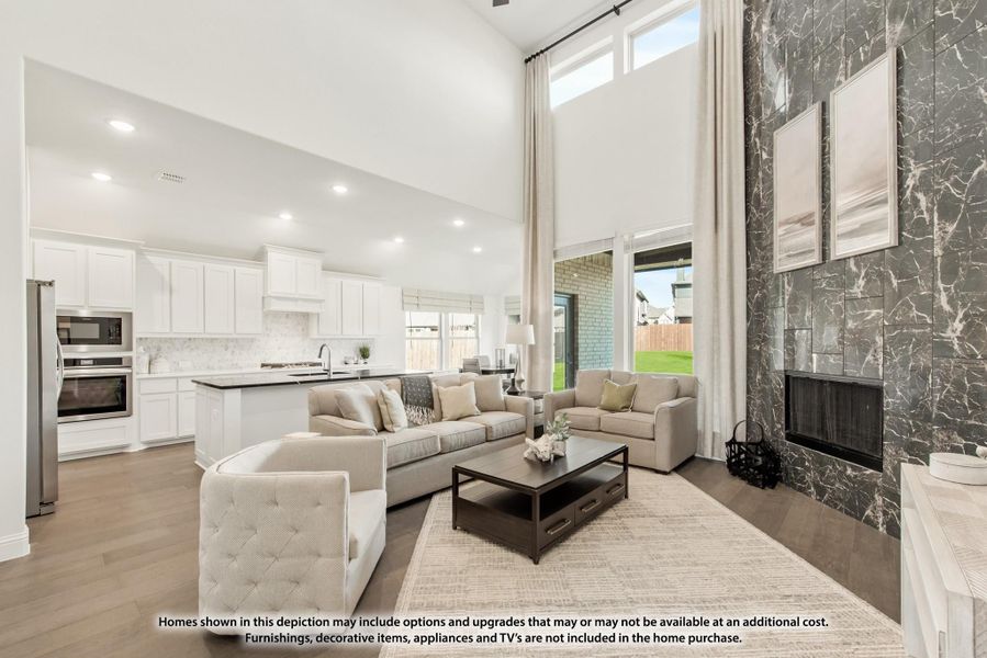 Open-concept living room with two-story ceiling, marble fireplace, and white kitchen in background Open-concept living room with two-story ceiling, marble fireplace, and white kitchen in background