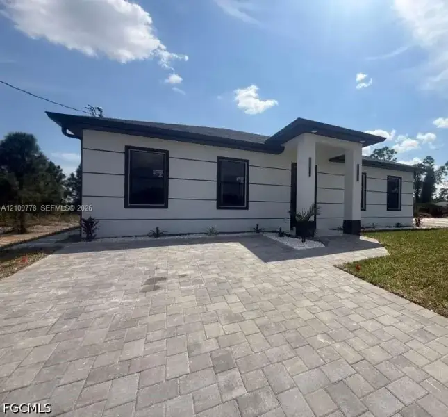 Modern exterior featuring white stucco finish with horizontal trim detailing, a covered entryway, and a paved brick driveway Modern exterior featuring white stucco finish with horizontal trim detailing, a covered entryway, and a paved brick driveway