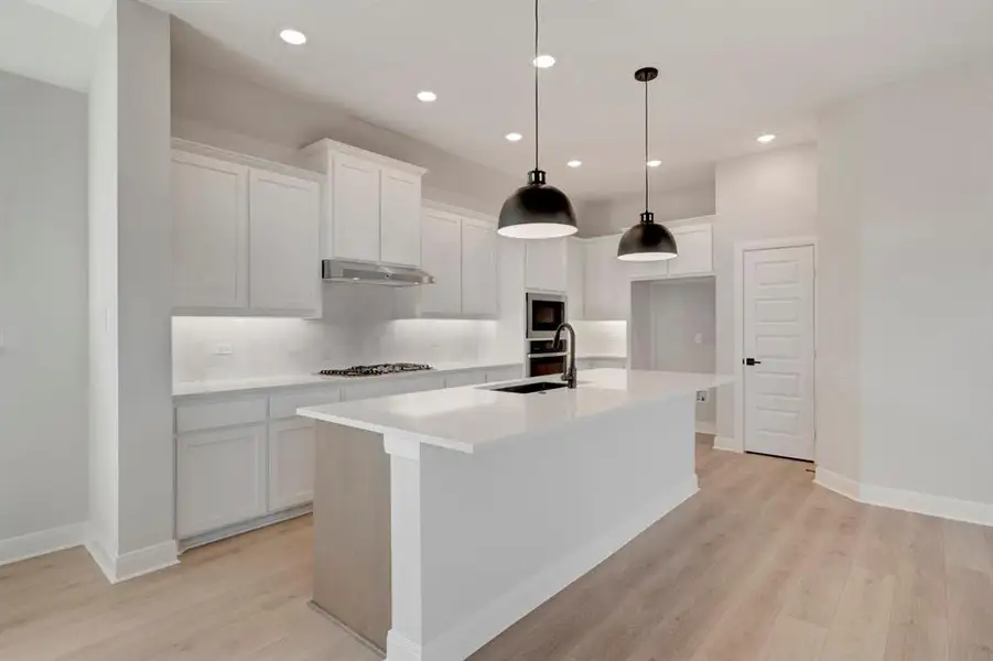 Kitchen with white cabinetry, a center island with sink, light wood finished floors, stainless steel appliances, and pendant lighting