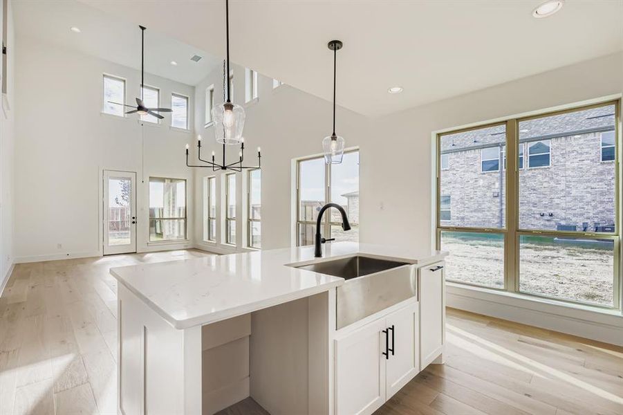 Kitchen featuring light wood finished floors, white cabinetry, pendant lighting, light stone counters, and a kitchen island with sink Kitchen featuring light wood finished floors, white cabinetry, pendant lighting, light stone counters, and a kitchen island with sink