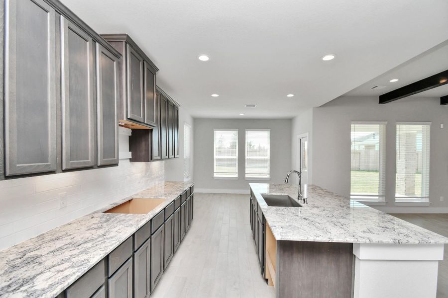 The kitchen is a culinary haven, featuring granite countertops, a tile backsplash, stainless steel appliances, 42” upper cabinets, and undercabinet lighting. Sample photo of completed home with similar floor plan. Actual colors and selections may vary. The kitchen is a culinary haven, featuring granite countertops, a tile backsplash, stainless steel appliances, 42” upper cabinets, and undercabinet lighting. Sample photo of completed home with similar floor plan. Actual colors and selections may vary.