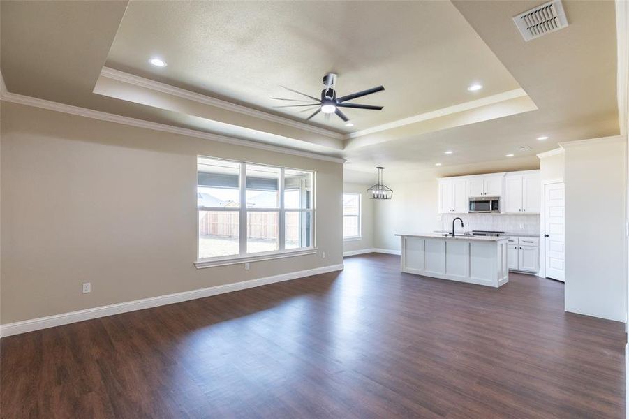 Open-concept living area featuring wood-finish flooring, a tray ceiling with recessed lighting, and a modern ceiling fan
