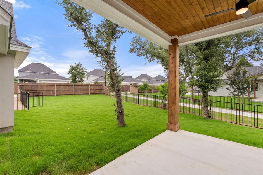 A spacious backyard with mature trees and a privacy fence borders a welcoming patio.