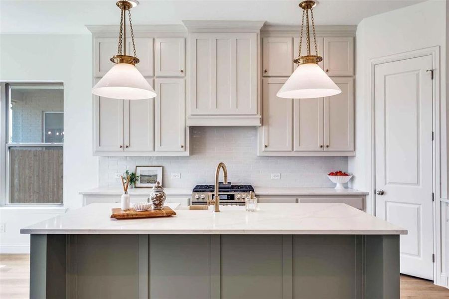 Kitchen featuring light wood-style floors, tasteful backsplash, a center island with sink, light stone counters, and decorative light fixtures Kitchen featuring light wood-style floors, tasteful backsplash, a center island with sink, light stone counters, and decorative light fixtures