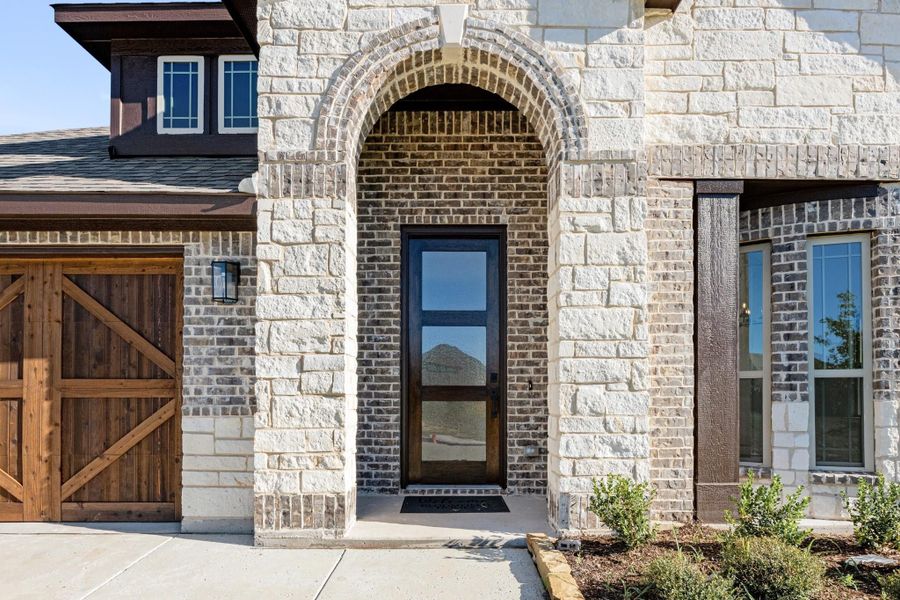 Home entrance with brick arched doorway, glass front door, stone exterior, and wood garage door nearby.