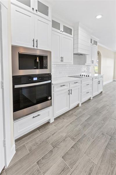 Kitchen featuring custom exhaust hood, appliances with stainless steel finishes, white cabinets, and decorative backsplash