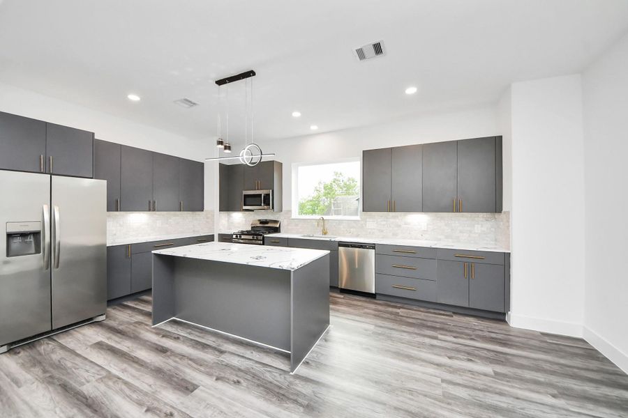 This modern kitchen features sleek gray cabinetry, stainless steel appliances, and a central island with a marble countertop. The space is well-lit with recessed lighting and a large window, complemented by light wood flooring. This modern kitchen features sleek gray cabinetry, stainless steel appliances, and a central island with a marble countertop. The space is well-lit with recessed lighting and a large window, complemented by light wood flooring.