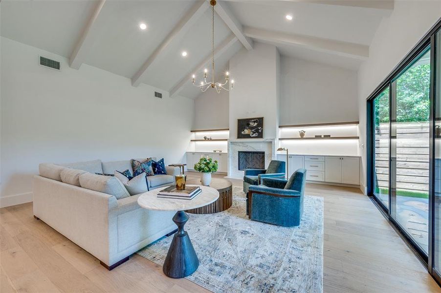 Living room with high vaulted ceiling, beam ceiling, a chandelier, light wood-style floors, and a fireplace Living room with high vaulted ceiling, beam ceiling, a chandelier, light wood-style floors, and a fireplace