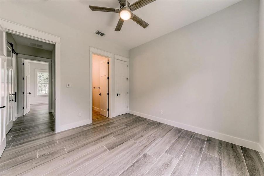 Unfurnished bedroom with light hardwood / wood-style flooring, a barn door, and ceiling fan