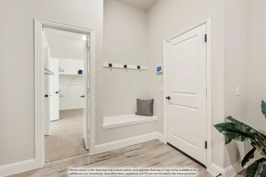 Mudroom with built-in bench, wall hooks, and light wood floors, with view into walk-in closet