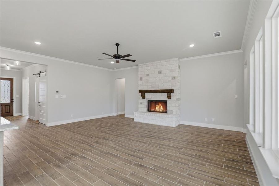 Unfurnished living room with a barn door, wood finish floors, a ceiling fan, recessed lighting, and ornamental molding