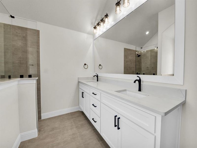Bathroom featuring double vanity, a sink, baseboards, and tiled shower Bathroom featuring double vanity, a sink, baseboards, and tiled shower