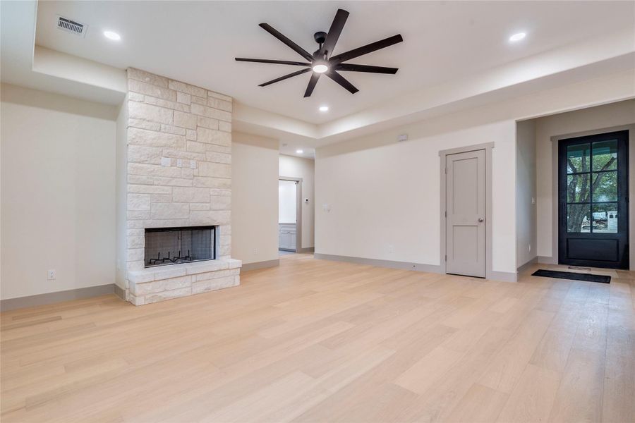 Unfurnished living room featuring ceiling fan, light wood-style floors, a stone fireplace, and recessed lighting