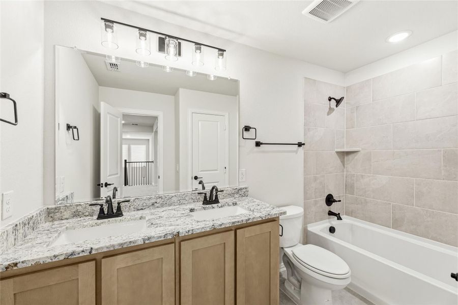 Bathroom with double sink vanity, granite countertop, and tiled shower-tub combo with black fixtures