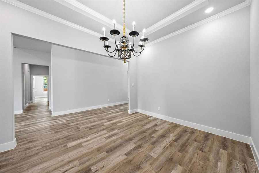 Empty room featuring crown molding, wood finished floors, a raised ceiling, and a chandelier