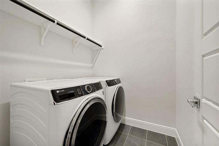 Laundry area featuring a front-load washer and dryer, white shelving with a hanging rod, and dark gray square tile flooring
