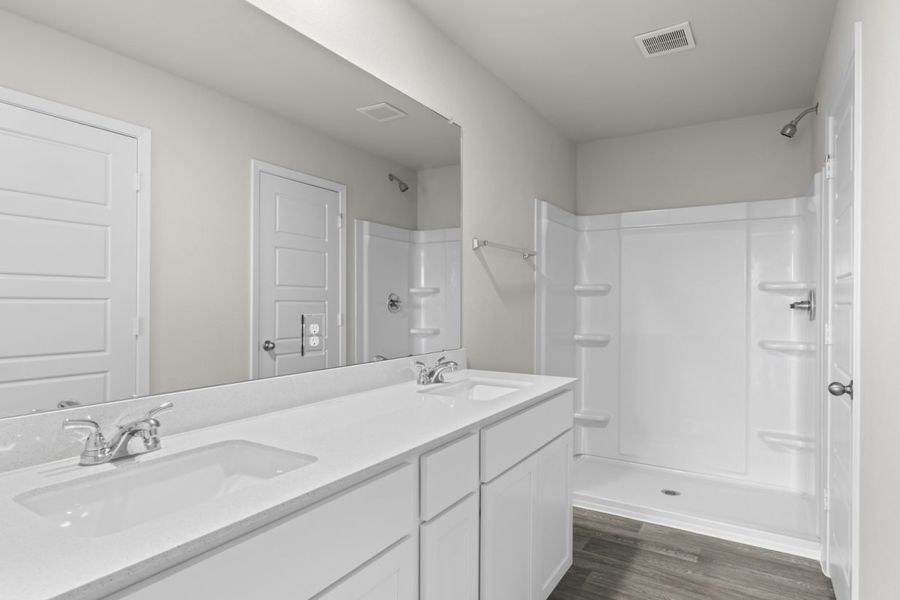 Image of a bathroom with a white jack and jill vanity, white cabinets, a large mirror, and a walk-in shower