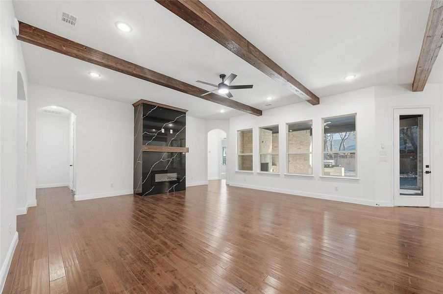 Unfurnished living room featuring arched walkways, hardwood / wood-style flooring, beamed ceiling, ceiling fan, and recessed lighting