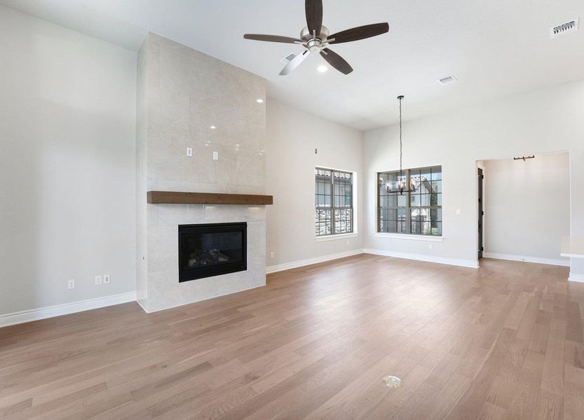 Unfurnished living room with wood finished floors, a ceiling fan, a chandelier, and a fireplace