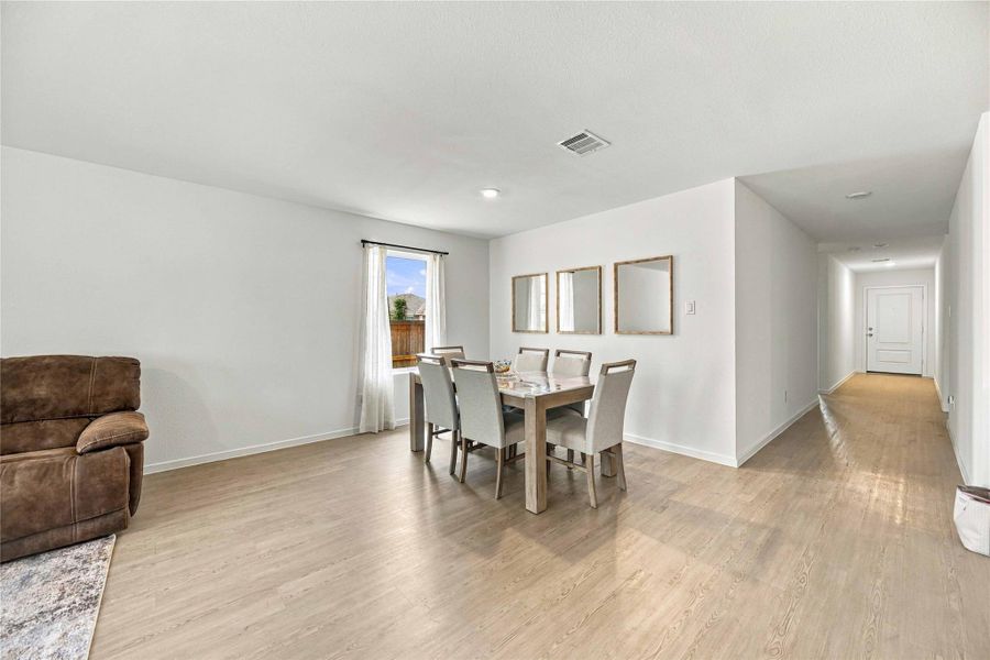 Spacious dining area with natural light streaming through a large window, featuring sleek hardwood floors and an inviting open layout.