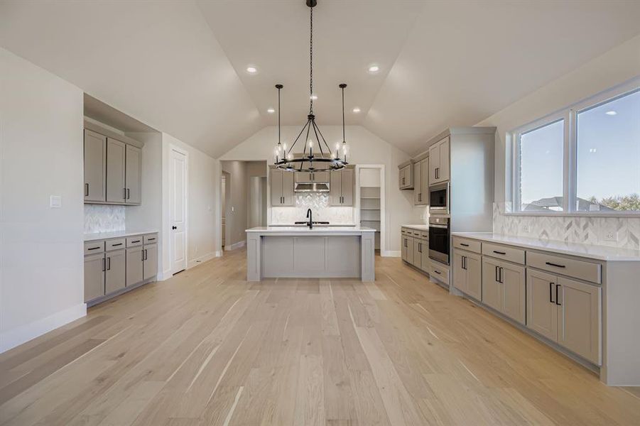 Kitchen with gray cabinets, decorative backsplash, a chandelier, vaulted ceiling, and recessed lighting