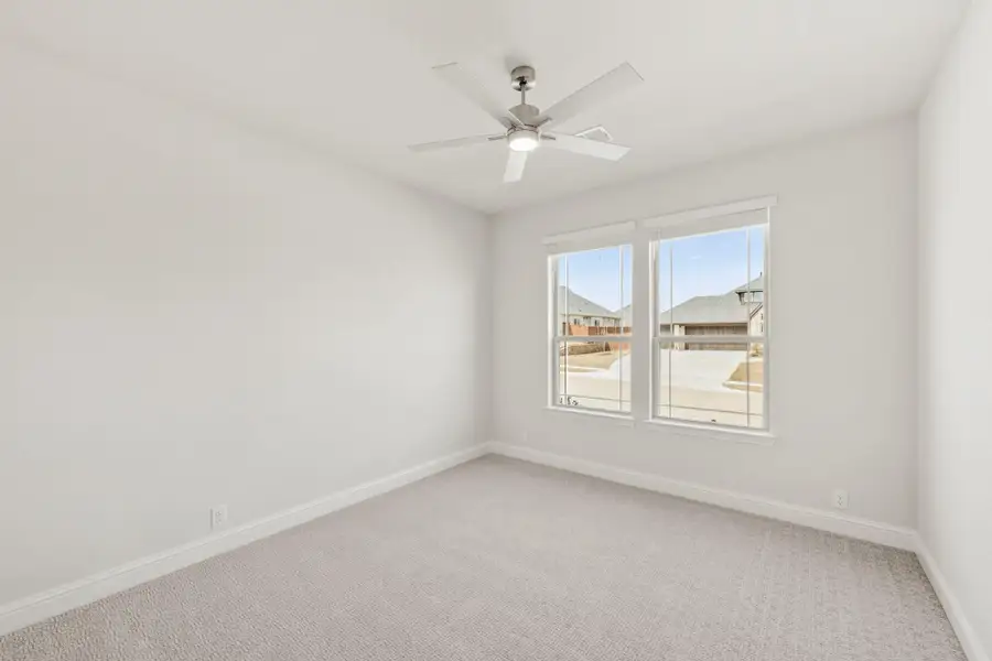 Empty bedroom with carpet flooring, ceiling fan, and double window overlooking neighborhood street