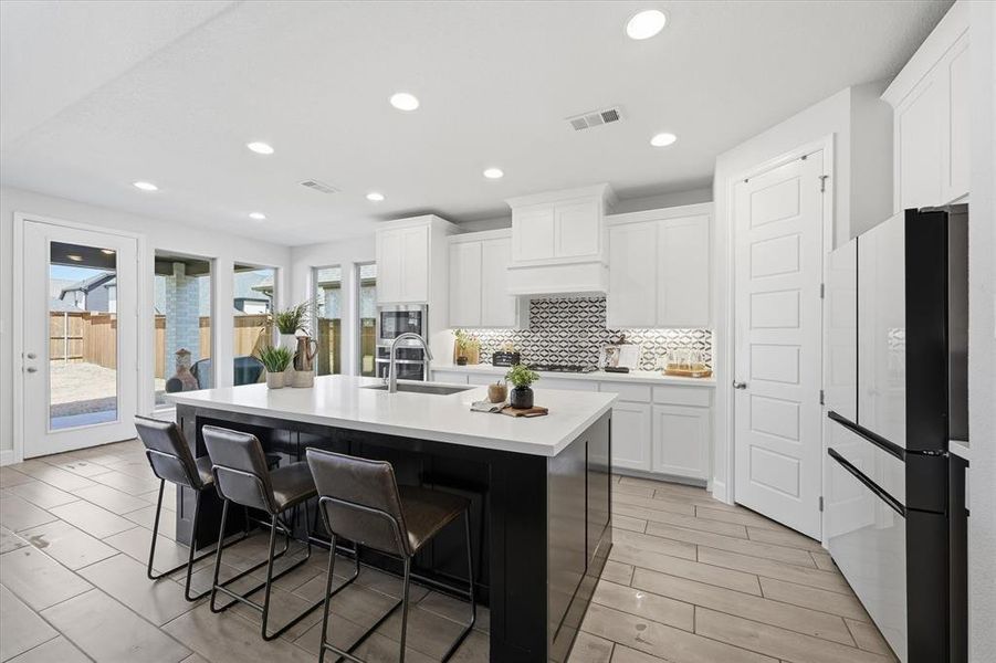Dual tone kitchen with stainless steel appliances, a breakfast area, a large island with farmhouse sink, and wood finish floors