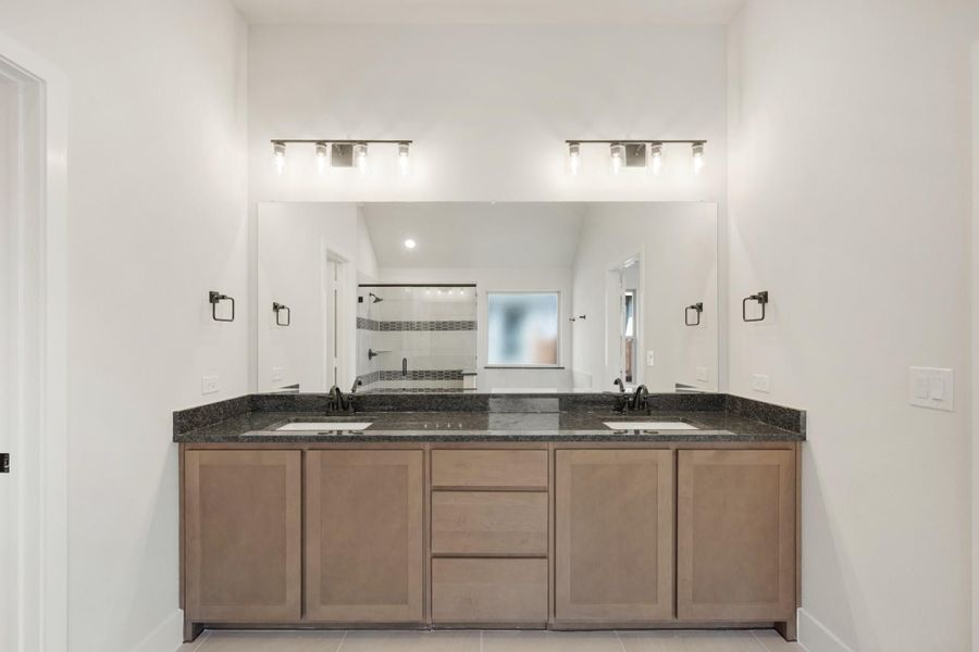 Bathroom double vanity with dark granite countertop, wood cabinets, dual sinks, and large mirror with overhead lighting