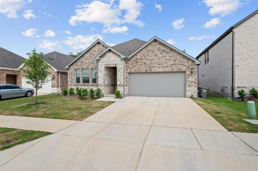 Brick and stone facade residence featuring an attached two-car garage, covered entry, front landscaping, and a concrete driveway Brick and stone facade residence featuring an attached two-car garage, covered entry, front landscaping, and a concrete driveway