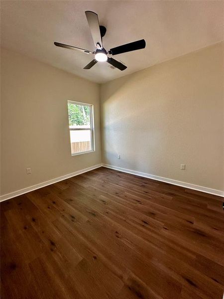 Room featuring wood-finish flooring, a window with exterior visibility, a modern ceiling fan with integrated lighting, and neutral wall tones