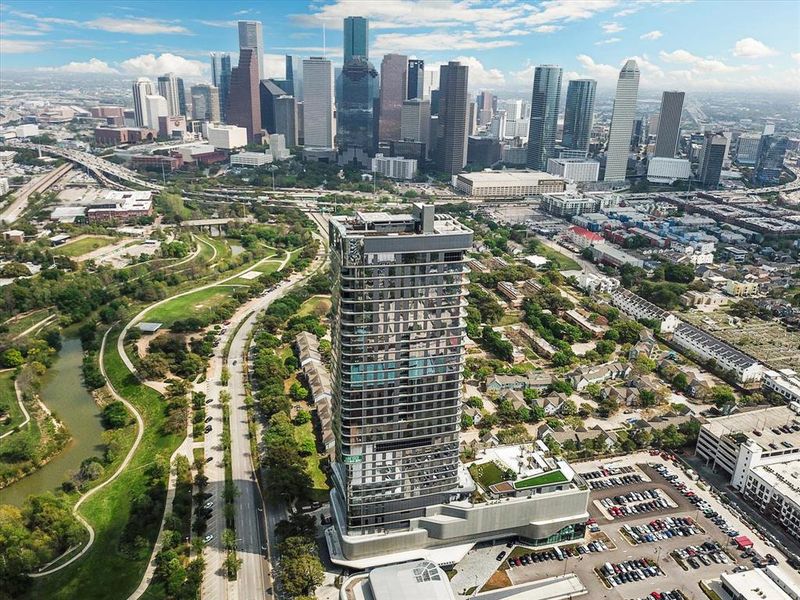 The Residences at The Allen, Houston’s premiere Luxury Condo Hotel Tower on Allen Parkway, Houston, stands gracefully against the city skyline. Its modern design and glass windows exude sophistication, while a warm glow from the setting sun highlights its elegance. Private balconies with lush greenery offer panoramic views of downtown Houston and Buffalo Bayou Park. This building embodies luxury living, with exceptional amenities and breathtaking vistas.