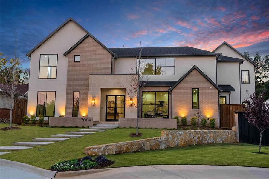 Contemporary two-story residence featuring a stucco and brick exterior, dark-framed windows, a stone accent entry, and a multi-tiered concrete walkway