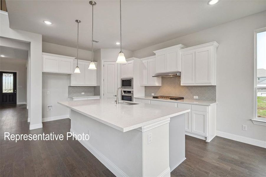 Kitchen featuring a large central island with pendant lighting, white cabinetry, integrated appliances, a tiled backsplash, and wood-finish flooring