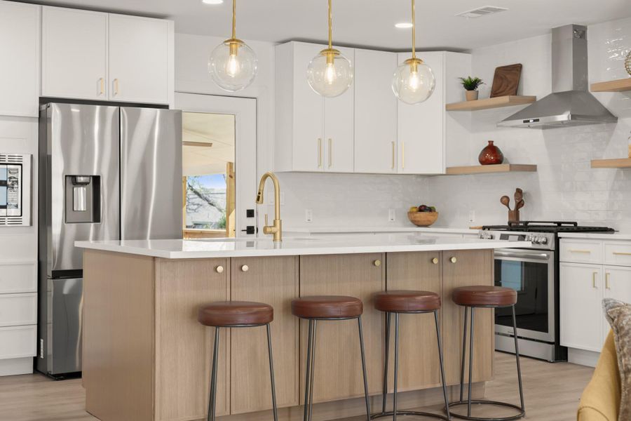 Kitchen featuring stainless steel appliances, a kitchen island with sink, two tone cabinetry, hanging light fixtures, and a kitchen bar