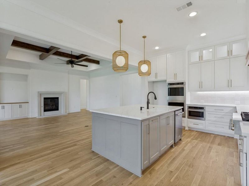 Open-concept kitchen featuring a large island with a countertop sink and matte black faucet, white shaker cabinetry with gold-toned hardware, and stainless steel built-in appliances Open-concept kitchen featuring a large island with a countertop sink and matte black faucet, white shaker cabinetry with gold-toned hardware, and stainless steel built-in appliances