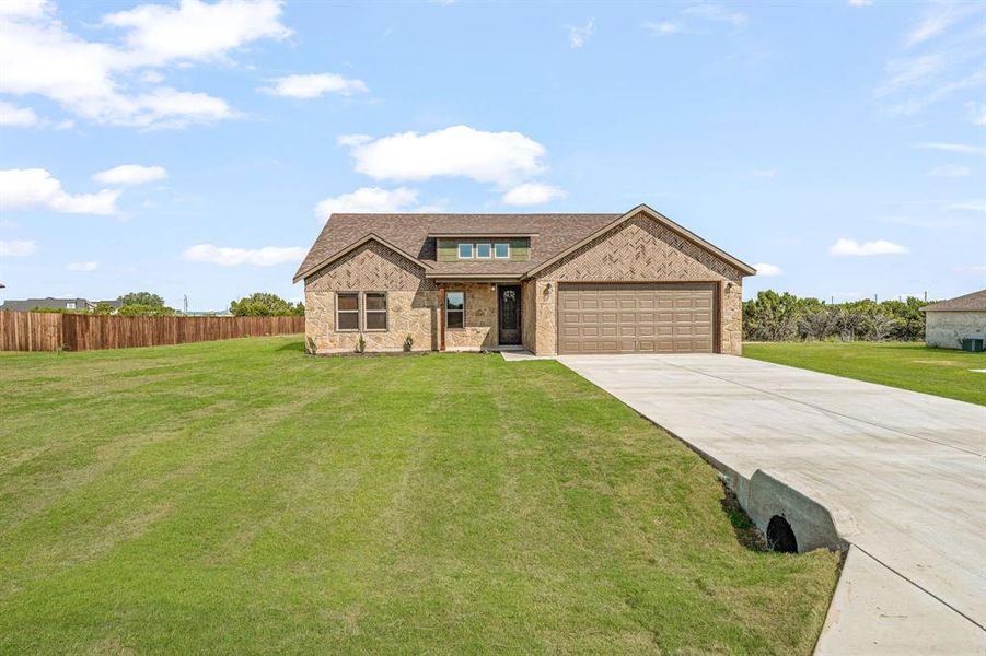 View of front of property with a front lawn, concrete driveway, a shingled roof, and brick siding