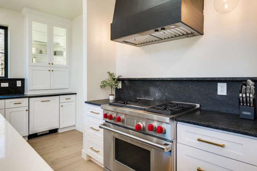 Kitchen with backsplash, designer stove, custom range hood, white cabinetry, and dishwashing machine