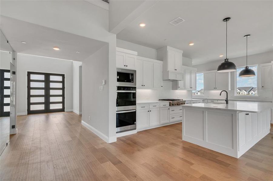 Kitchen with light hardwood / wood-style floors, a kitchen island with sink, sink, white cabinetry, and appliances with stainless steel finishes