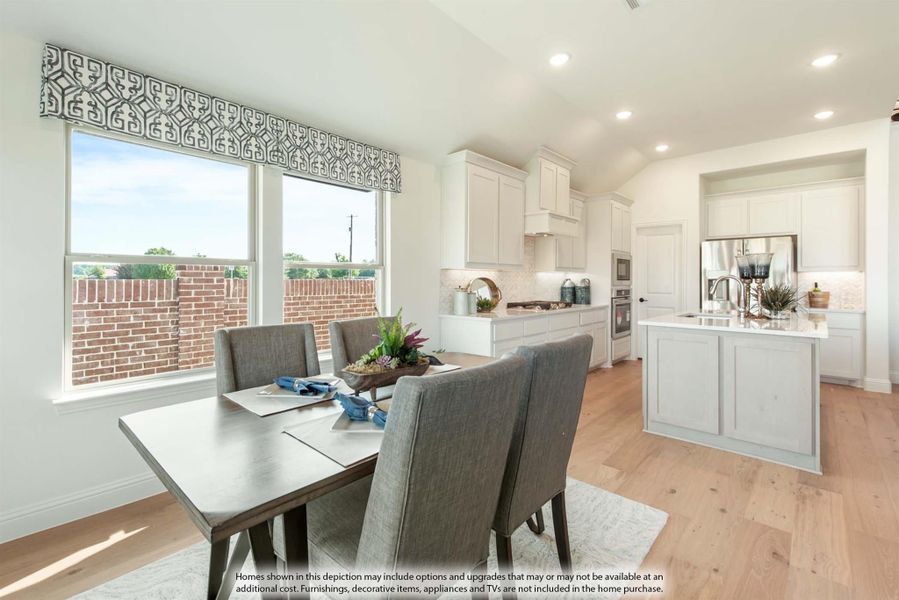 Open dining area with gray chairs flows into kitchen with white cabinets and center island on light hardwood floors
