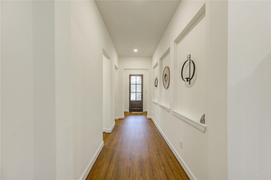 Bright, welcoming hallway with wooden flooring and decorative wall niches, leading to a glass-paneled door.