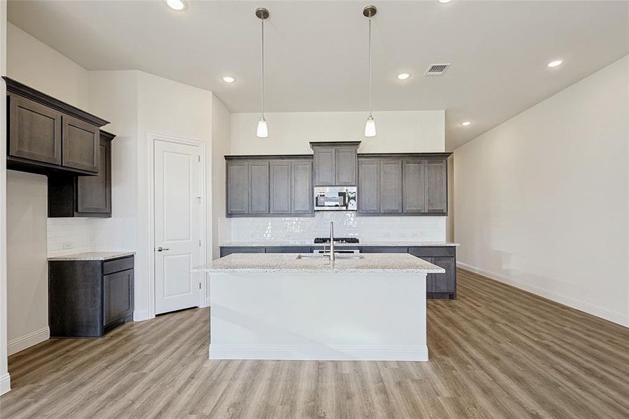 Kitchen featuring backsplash, light stone countertops, a center island with sink, and hanging light fixtures