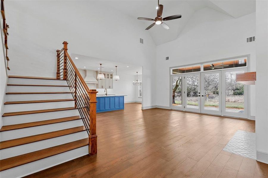 Unfurnished living room with ceiling fan with notable chandelier, high vaulted ceiling, sink, and light hardwood / wood-style floors