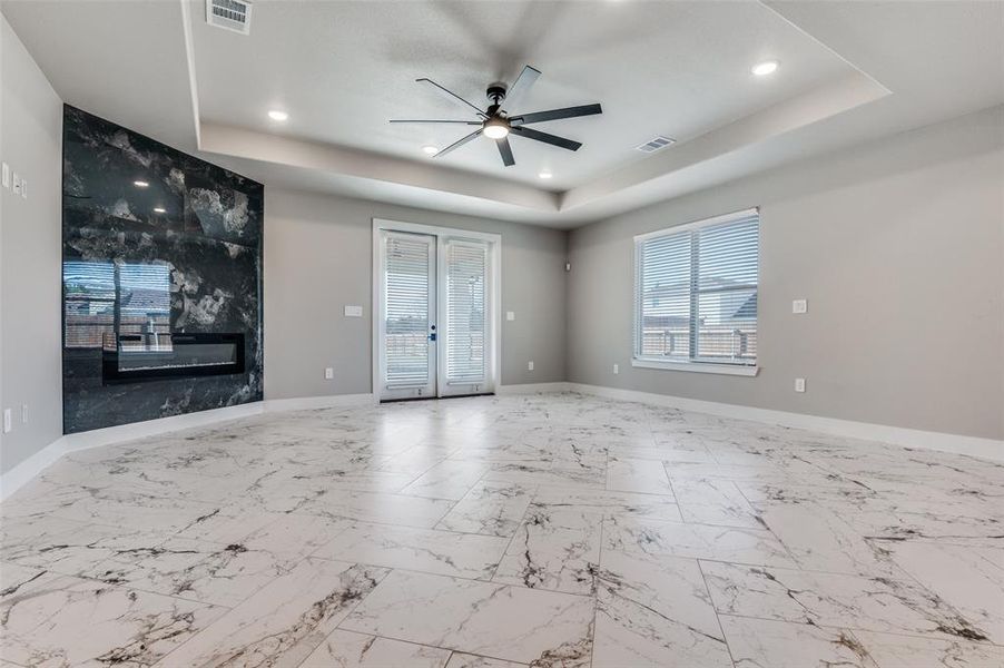 Unfurnished living room featuring marble finish flooring, a fireplace, a raised ceiling, a ceiling fan, and recessed lighting