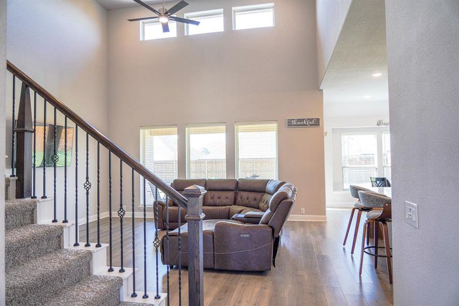 Living room featuring plenty of natural light, wood finished floors, a ceiling fan, a towering ceiling, and stairway
