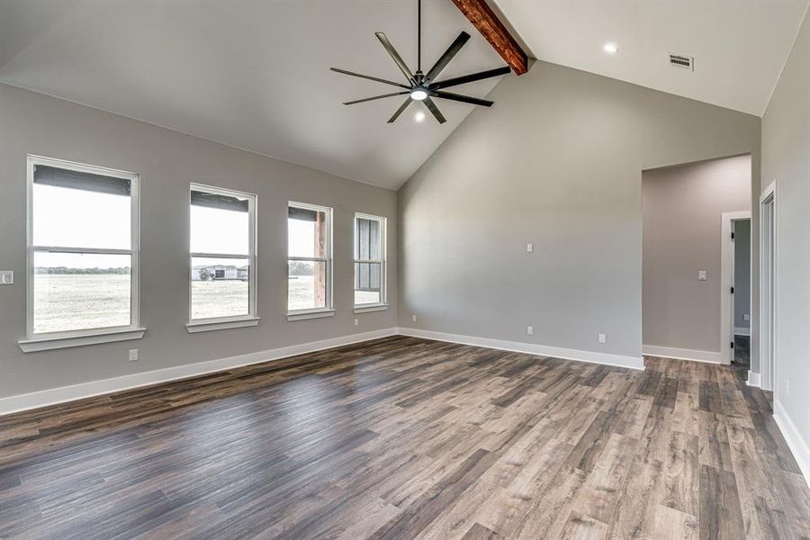 Unfurnished living room featuring high vaulted ceiling, beamed ceiling, ceiling fan, and dark wood-type flooring